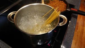 A pot with boiling water and spaghetti sticking out.