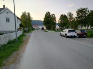 En gate med hus på venstre side, og to parkerte biler og en kirke på høyre side.