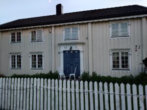 Et hvitt hus med blå ytterdør. Tallene 17 og 73 står over døra.