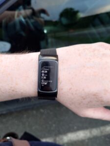 En arm med et sort treningsarmband (FitBit) på. Det viser tiden (44:39), distansen (3,2 km), og gjennomsnittsfart (13'58").