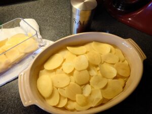 Sliced potatoes in a ovenproof dish, and in a mandoline.