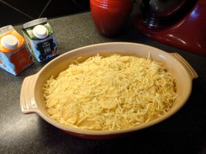 An ovenproof dish with sliced potatoes and grated cheese.