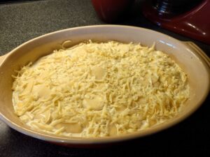 An ovenproof dish with sliced potatoes, grated cheese, and cream.