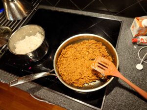 A saucepan with boiled rice and a skillet with minced meat mixed with tomato puree and heavy cream.