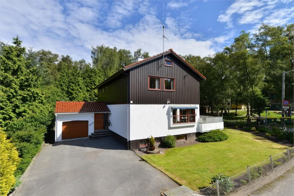 Et hvitt og mørkebrunt hus med garasje. gårdsplass, og grønn plen.