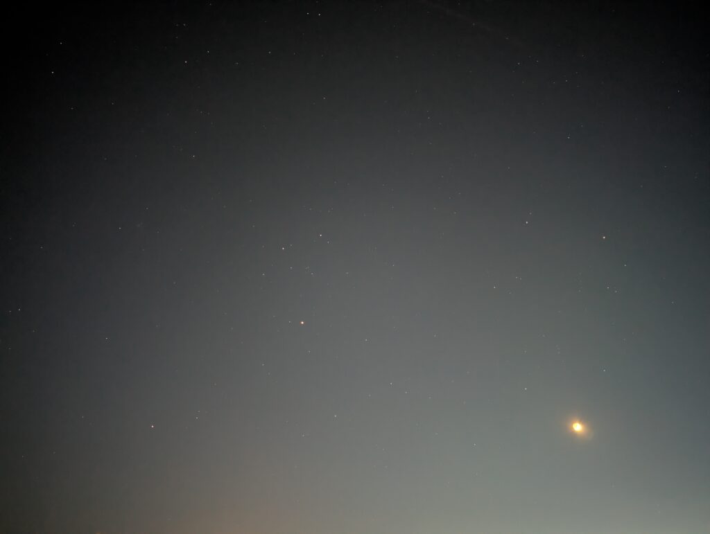 En himmel full av stjerner, et lysende punkt i nedre høyre hjørne, og lysforurensing.